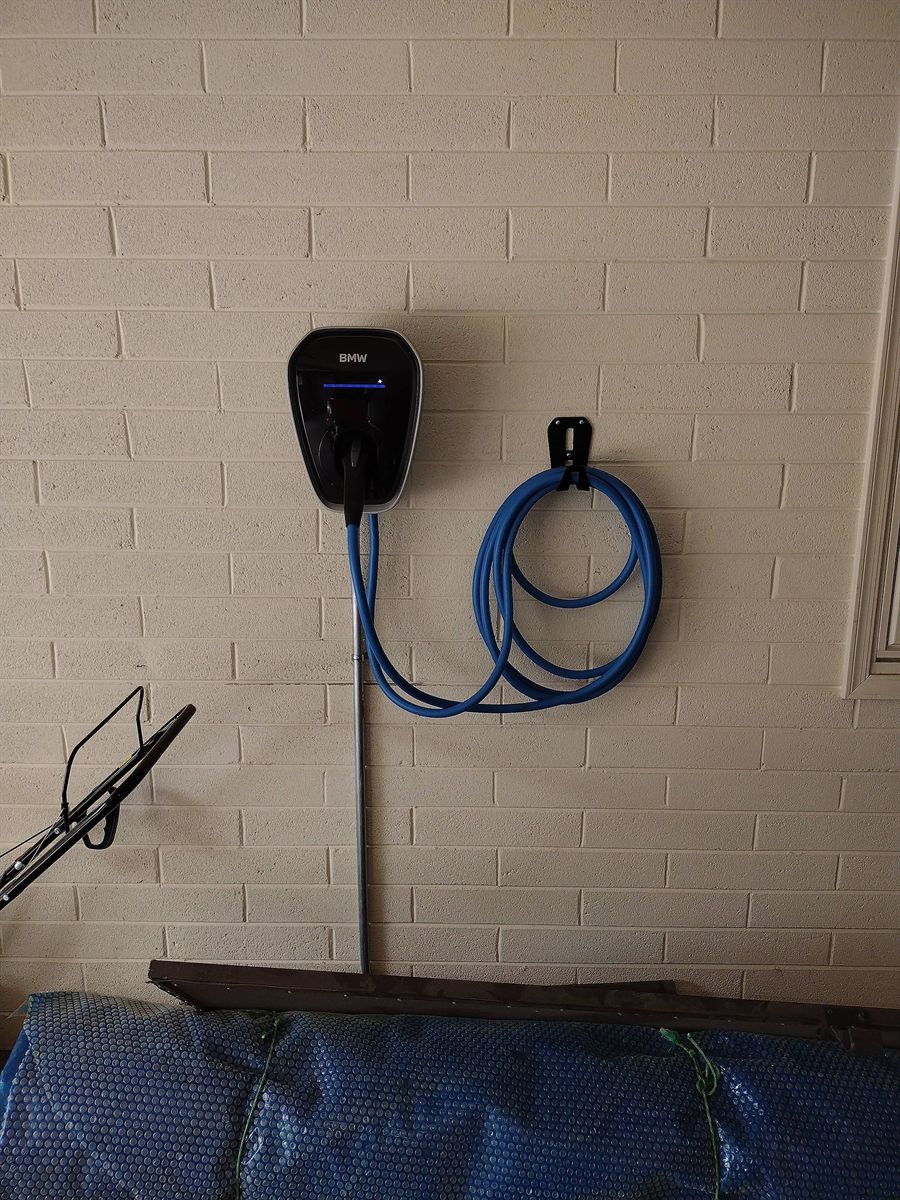 BMW wall charger installed on a painted brick wall with a cable hook