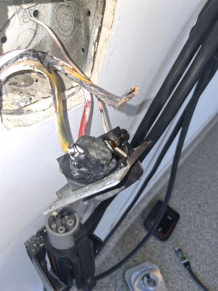 A melted 14-50 charging outlet with scorched wires, pulled from the wall beside an EV charger plug