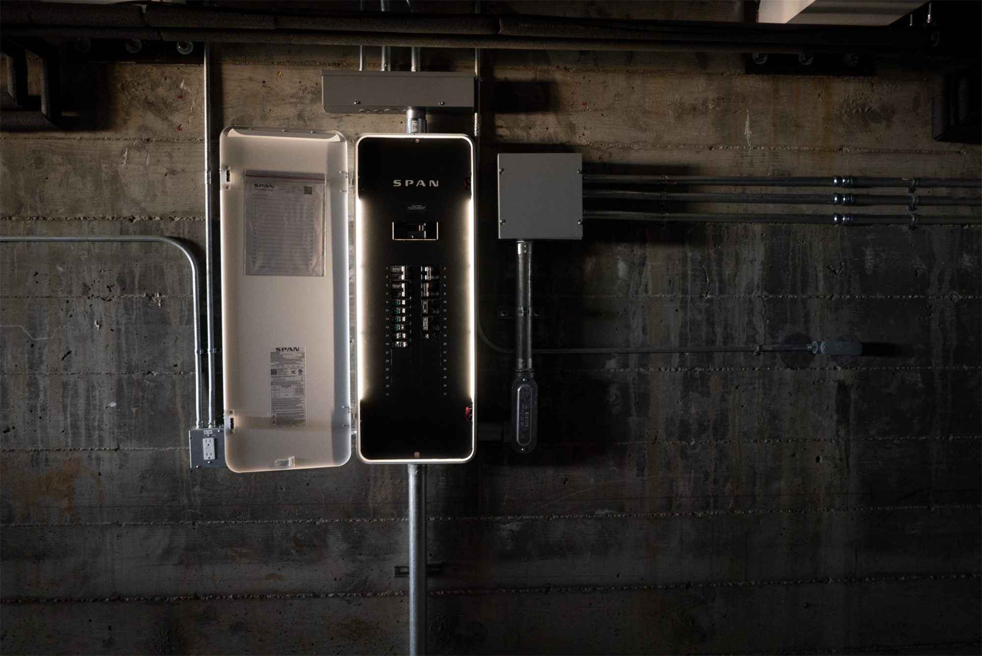 SPAN Panel installed on a concrete wall with its door open and interior lights on