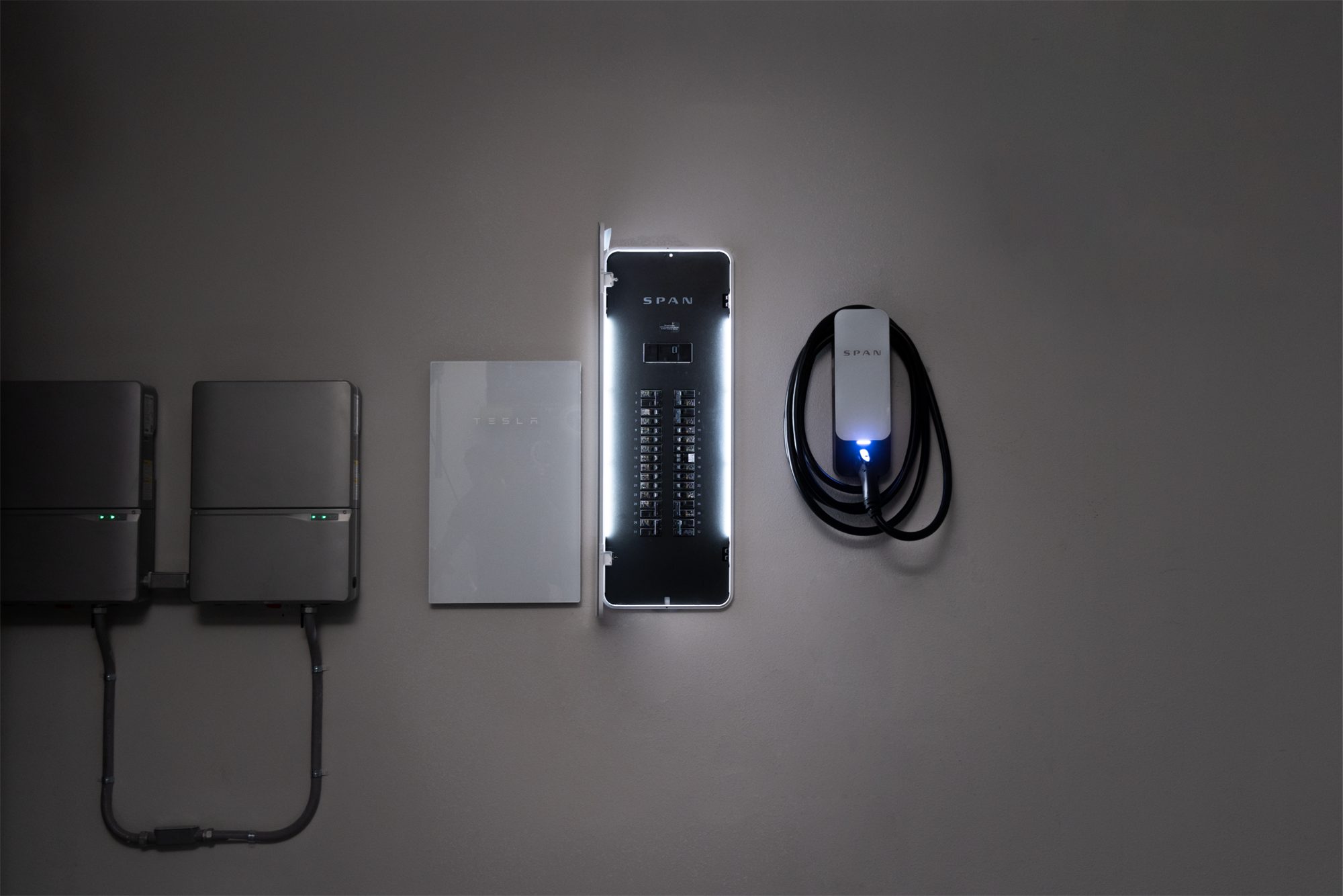 SPAN Panel with lights on, installed beside a Tesla Powerwall, inverters and a SPAN Drive EV charger