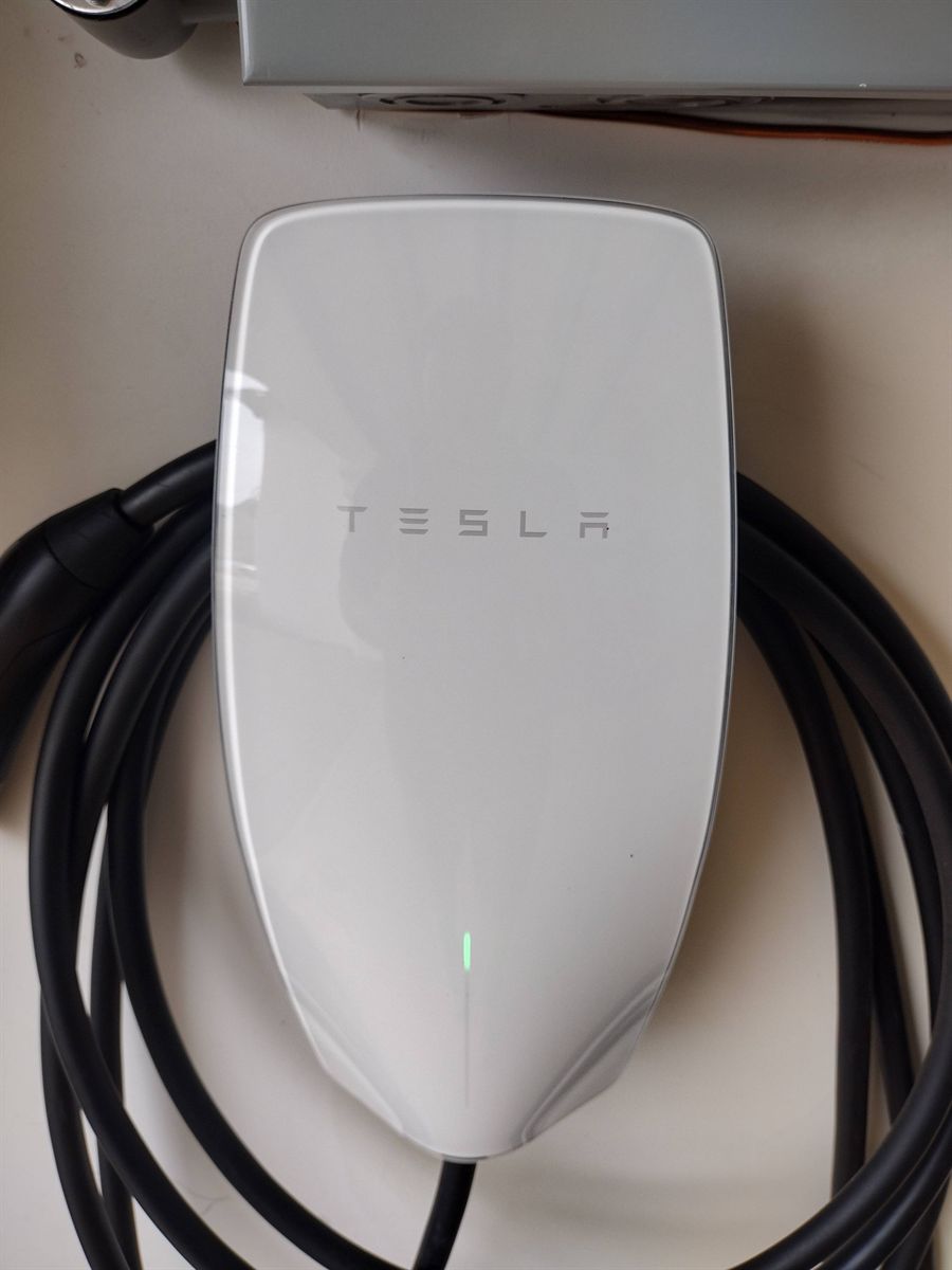 Close-up of a Tesla Wall Connector with its status light on and the charging cable coiled