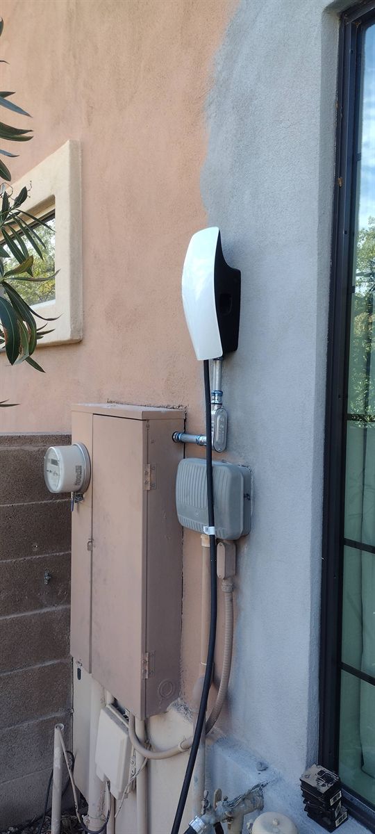 Tesla Wall Connector mounted on an exterior wall next to the electric meter and disconnect