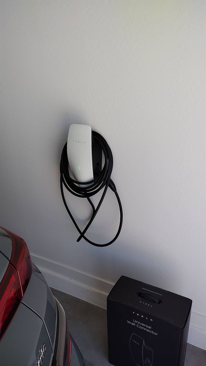 Tesla Universal Wall Connector on a garage wall beside a parked Tesla, with its box on the floor