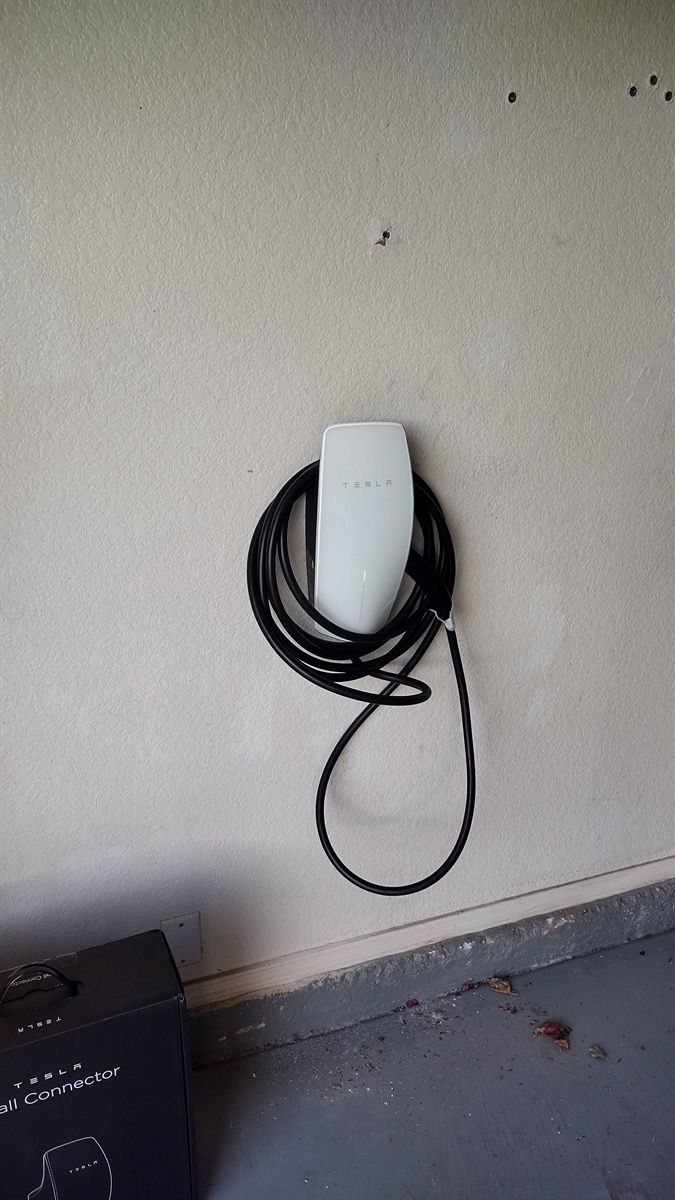 Newly installed Tesla Wall Connector in a garage with its Tesla box on the floor